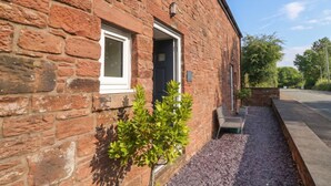A brick building with a door and windows, a small tree, and a gravel path. - Coney Garth Cottage (Beckermet)
