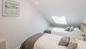 A bedroom with two beds, a skylight, and a framed picture on the wall. - Coney Garth Cottage (Beckermet)