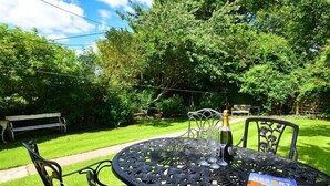 Ein runder Metalltisch mit Stühlen, einer Champagnerflasche und einer Broschüre in einem üppigen Garten.