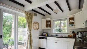 A modern kitchen with white cabinetry, a black countertop, and a window overlooking a garden. - Little Berwick Cottage (Dorchester)