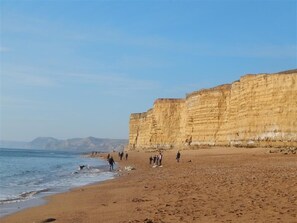 A beach with people walking along the shore, cliffs in the background, and the ocean. - Little Berwick Cottage (Dorchester)
