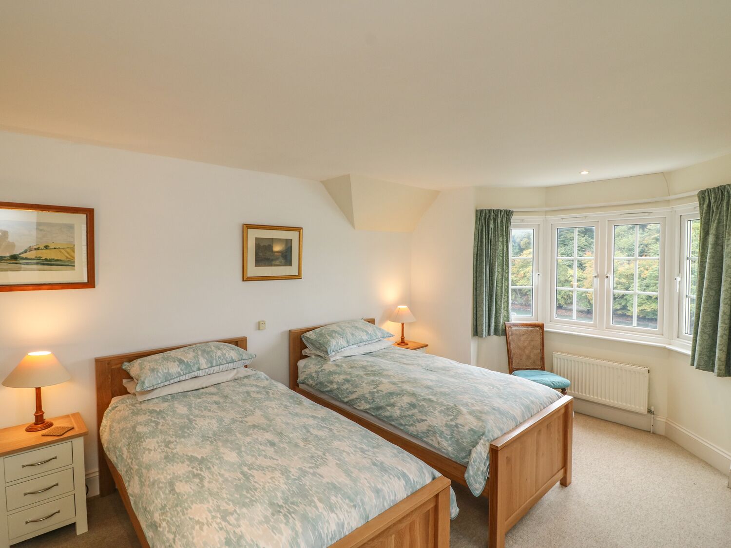 A bedroom with two single beds, a nightstand with a lamp, a framed picture on the wall, and a window with curtains.