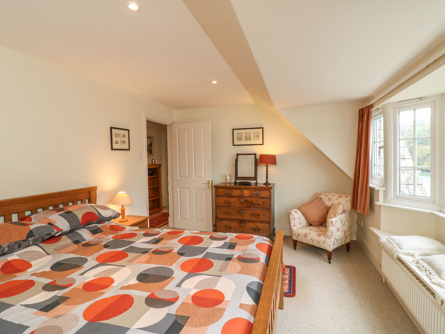 Une chambre à coucher avec un lit, une commode, une chaise et une fenêtre avec des rideaux.