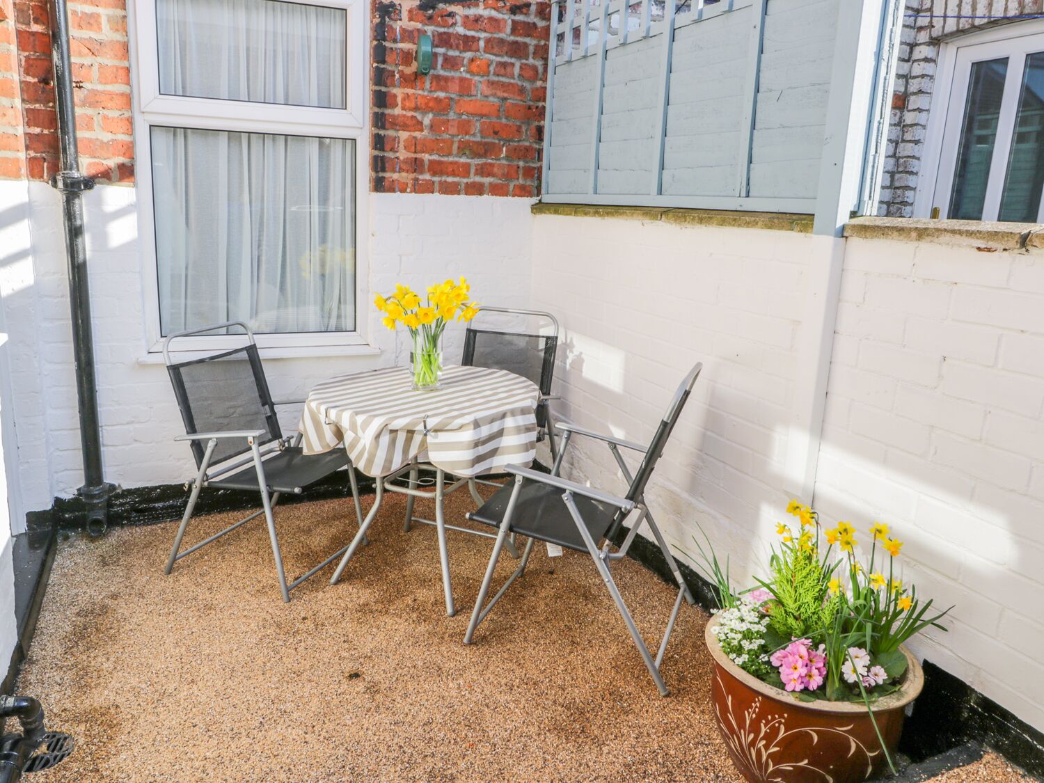 A small patio with a table and chairs, a potted plant with flowers, and a brick wall.