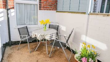 A small patio with a table and chairs, a potted plant with flowers, and a brick wall.