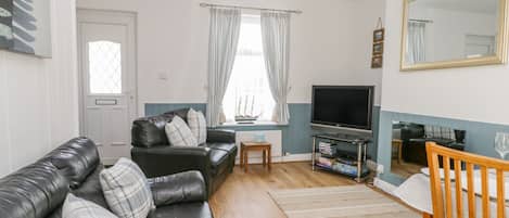 A living room with a black leather sofa, a wooden chair, a TV, and a bookshelf.