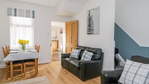 A modern living room with a dining area, a black leather sofa, and a staircase. - Sea Breakers Cottage (Filey)