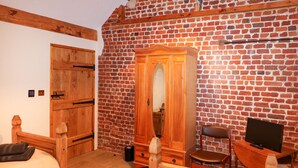 A room with two wooden beds, a wooden wardrobe, a television, and a brick wall. - Honey Buzzard Barn (Fakenham)