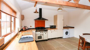 A kitchen with wooden beams, a stove, a microwave, and a washing machine. - Honey Buzzard Barn (Fakenham)
