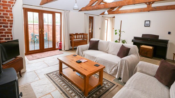 A cozy living room with a sofa, a wooden coffee table, a piano, and a brick wall. - Honey Buzzard Barn (Fakenham)