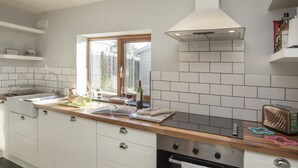 Une cuisine moderne avec des meubles blancs, un plan de travail en bois, un four encastré et une fenêtre laissant entrer la lumière naturelle.