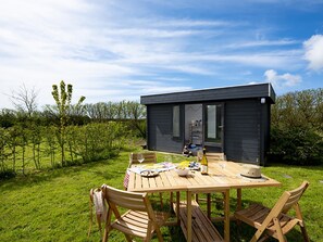 Une petite cabane en bois sombre, avec une table et des chaises placées à l’extérieur.