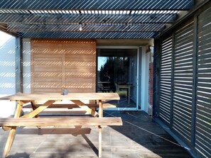 A wooden picnic table with a bench, a metal roof, and a garage door in the background. - La Gurlanne (Lasseran)