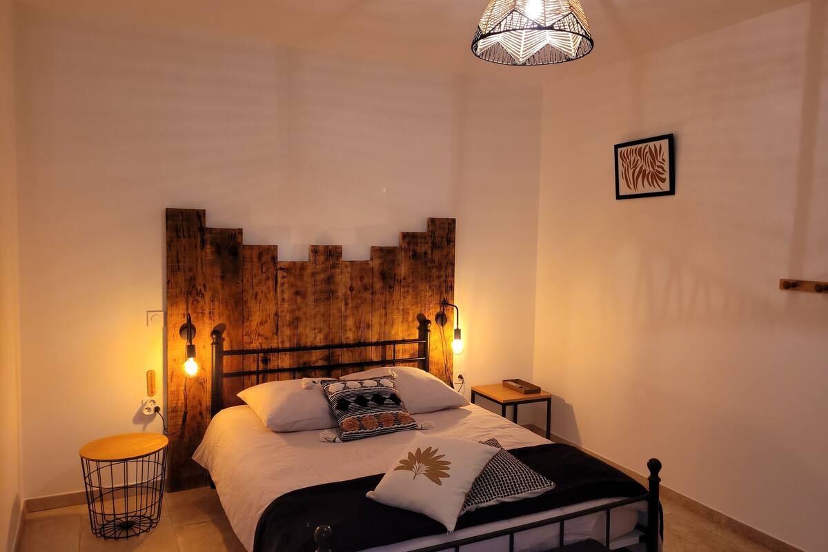 A bedroom with a wooden headboard, a bed with white bedding, a bedside table, and a hanging light fixture.