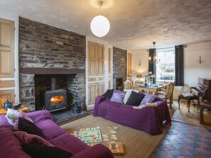 A cozy living room with a stone fireplace, a sofa, a dining table with chairs, and a piano. - 12 Victoria Terrace (Caernarfon)