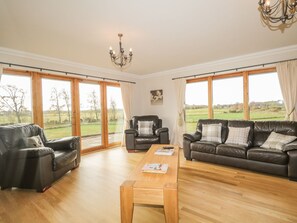 A spacious living room with a wooden coffee table, leather sofas, and a chandelier. - The Glebe (Invergordon)