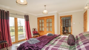Ein Schlafzimmer mit Bett, Stuhl, Holztür und Blick ins Freie.