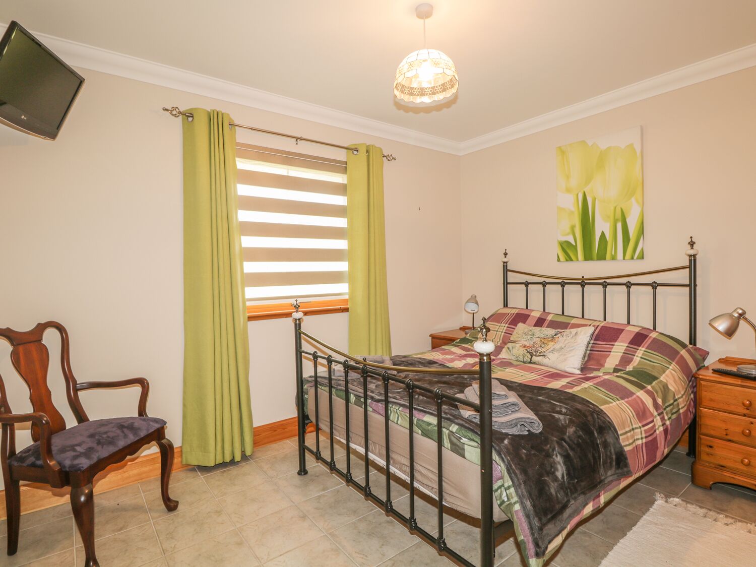A bedroom with a bed, a chair, a bedside table, a lamp, a painting, and a window with curtains.