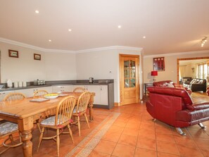 A spacious living area with a red leather sofa, a wooden dining table with chairs, a kitchen with a wooden door, and a tiled floor. - The Glebe (Invergordon)