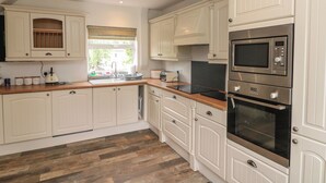 A kitchen with white cabinetry, a wooden countertop, a built-in oven, and a window with a view of greenery.