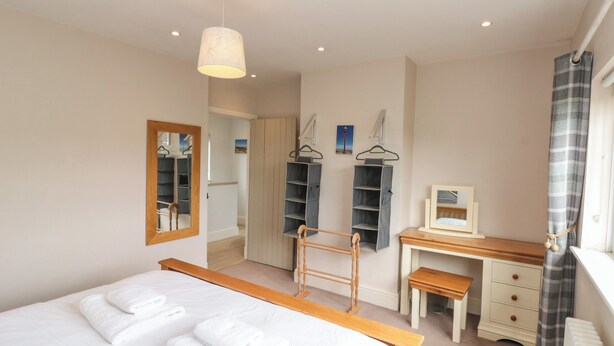 A bedroom with a bed, a wooden bench, a desk, and a mirror.