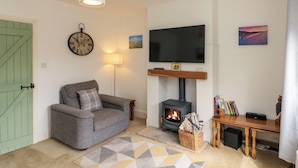 A cozy living room with a sofa, a fireplace, a TV, and a clock on the wall.