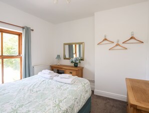 Ein Schlafzimmer mit Bett, Kommode, Spiegel und einem Fenster mit Vorhängen.