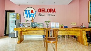 Una recepción con mostrador de madera, una silla, un refrigerador y una pared con el texto "GELORA Guest House".