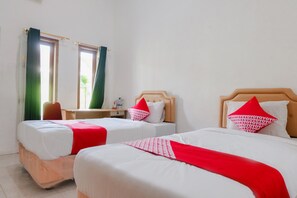 Une chambre d’hôtel avec deux lits, chacun recouvert d’une couvre-lit à motifs rouges et blancs, agrémentée d’oreillers blancs et dotée d’une tête de lit en bois. On y trouve une petite table avec une chaise, une table de chevet et une lampe.