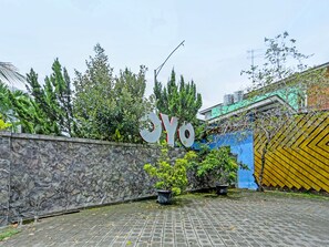 Un mur de pierres sur lequel est apposé un grand panneau avec les lettres « YO », des plantes en pot et un sol recouvert de carreaux.