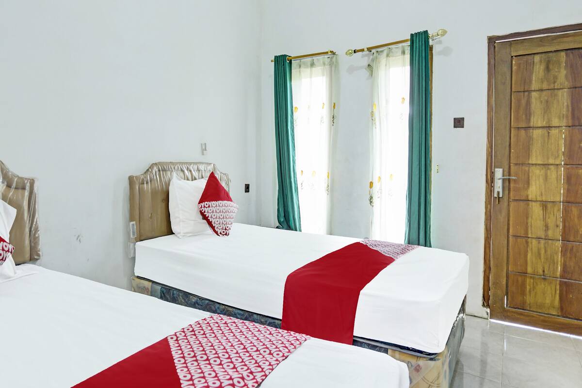 Dos camas individuales con ropa de cama blanca y roja, una puerta de madera y cortinas color turquesa.