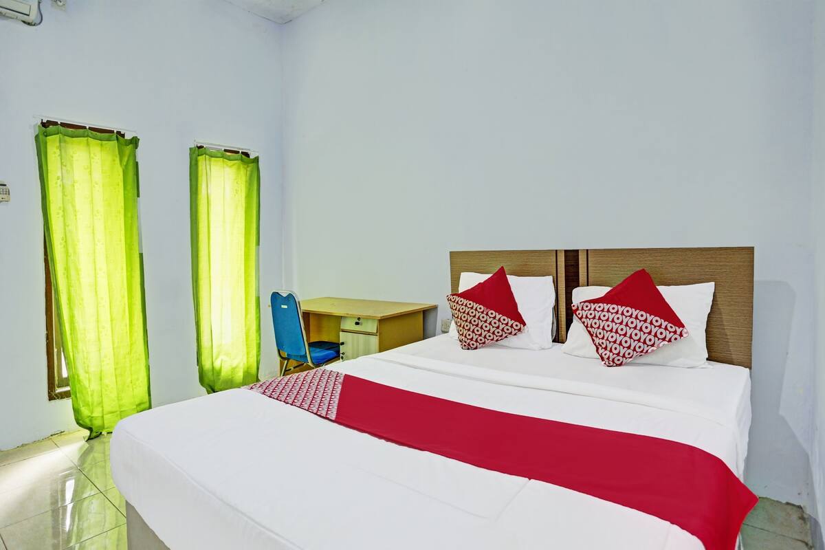 Habitación de hotel con cama, dos almohadas, escritorio y una silla.