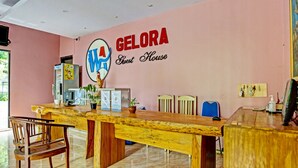 Un mostrador de recepción con encimera de madera, una silla y un letrero en la pared que dice "GELORA Guest House".