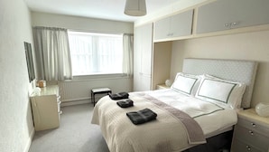 Une chambre bien rangée, avec un lit, des tables de chevet, un bureau et une fenêtre avec des rideaux.