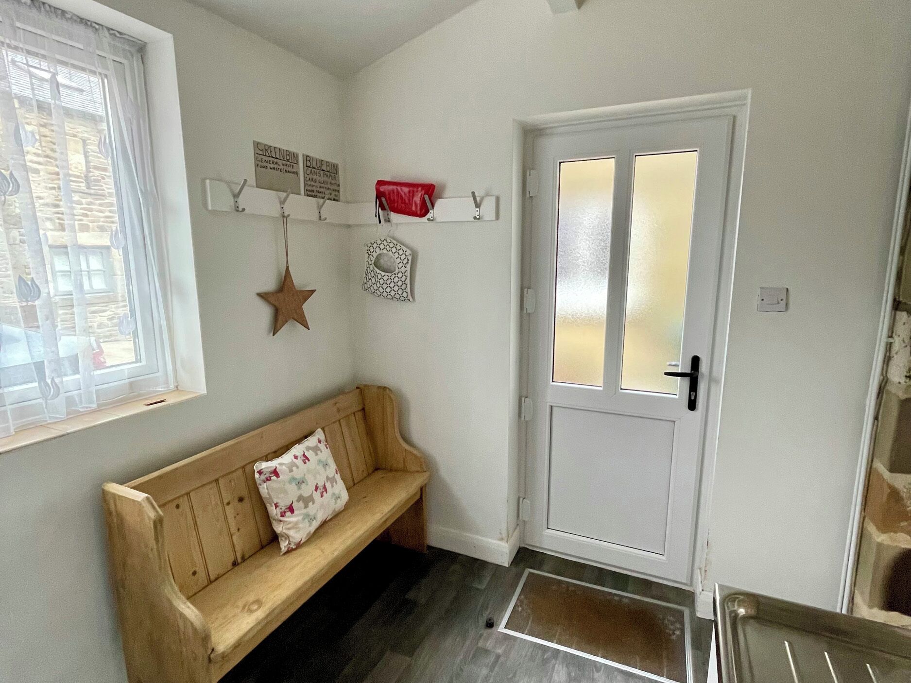 A hallway with a wooden bench, a white door with frosted glass panels, and wall-mounted signs for waste disposal.