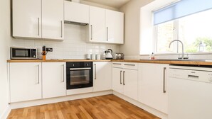 Une cuisine moderne avec des meubles blancs, un four à micro-ondes, un four traditionnel, un lave-vaisselle et une fenêtre donnant sur un paysage verdoyant.