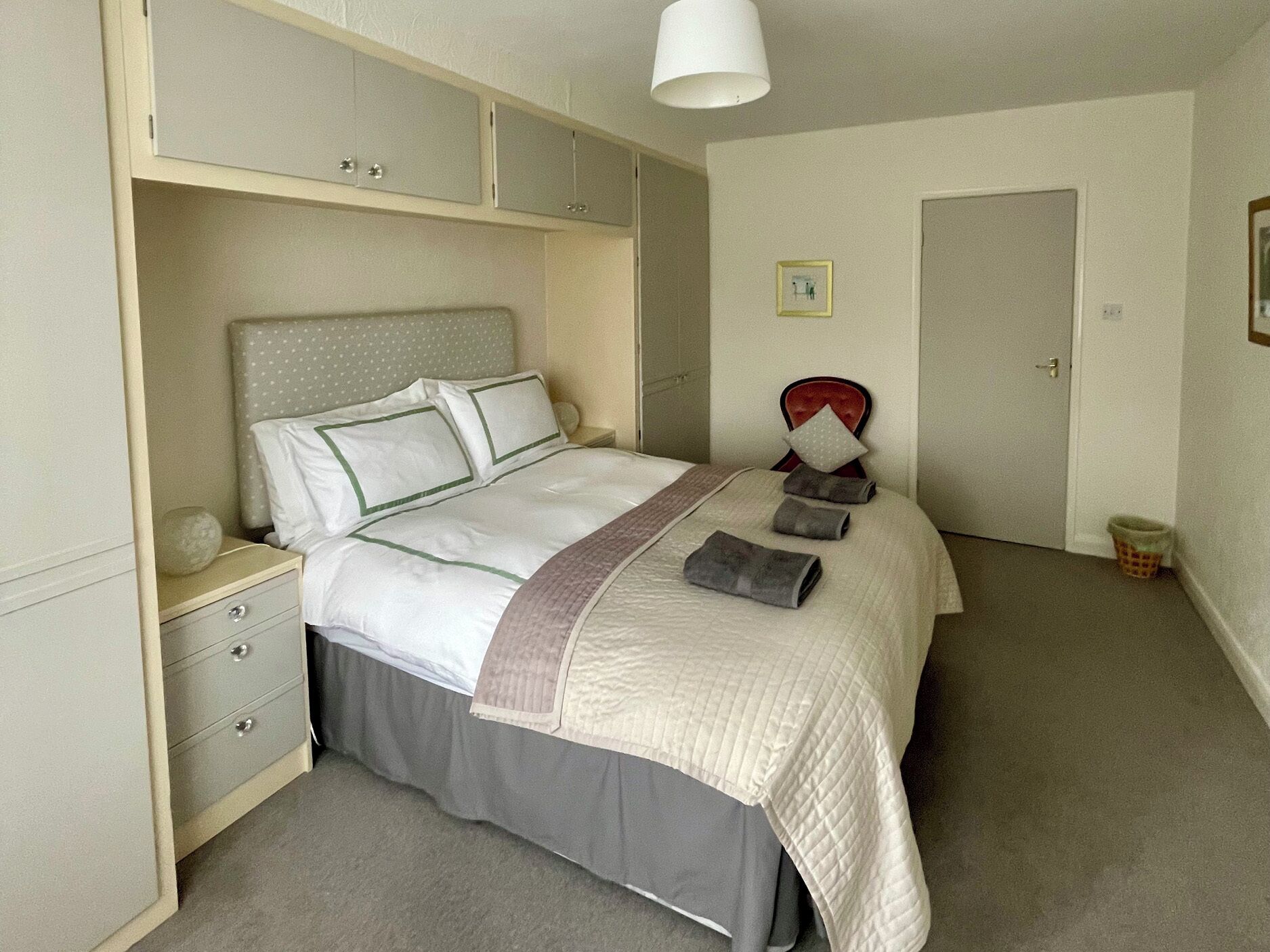 A neatly arranged bedroom with a bed, bedside tables, a wardrobe, and a door.