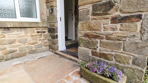 Une entrée en pierre avec une porte, un chemin en pierre et un jardinier.