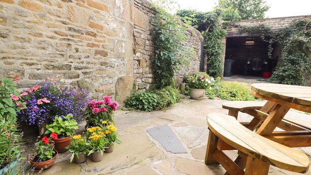 Une terrasse en pierre avec une table de pique-nique en bois et des plantes en pot.