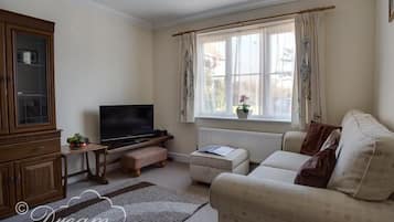 Ein Wohnzimmer mit Fernseher, Holzschrank, Sofa und einem Fenster mit Vorhängen.