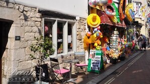 Une rue où se trouve un magasin vendant des jouets et des ballons de plage, une enseigne indiquant « Queen of Sports », et une autre indiquant « Dreams Cottages ».