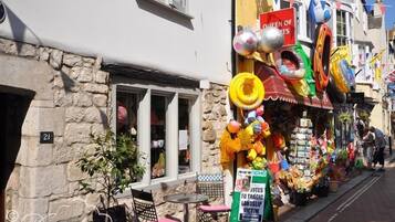 Una calle con una tienda que vende juguetes y balones de playa, un cartel que dice 'Queen of Sports' y un cartel de 'Dreams Cottages'.