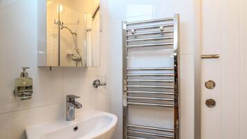 Un bagno con un lavandino bianco, uno specchio, un dispenser di sapone in vetro e un portaservizi cromato.