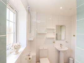 Un baño moderno con azulejos blancos, un inodoro, un lavamanos y una ventana.