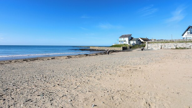 Une plage avec un mur de pierres et deux maisons.
