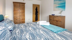 Une chambre à coucher avec un lit, une armoire en bois, un manteau accroché, un tableau et un bureau avec une lampe.