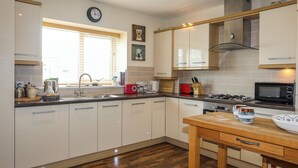 Une cuisine moderne avec des meubles blancs, un plan de travail en bois, une cuisinière à gaz, un four à micro-ondes et une fenêtre équipée de stores.
