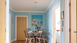 Un coin repas avec une table et des chaises en bois, un tableau accroché au mur et une porte donnant sur une autre pièce.