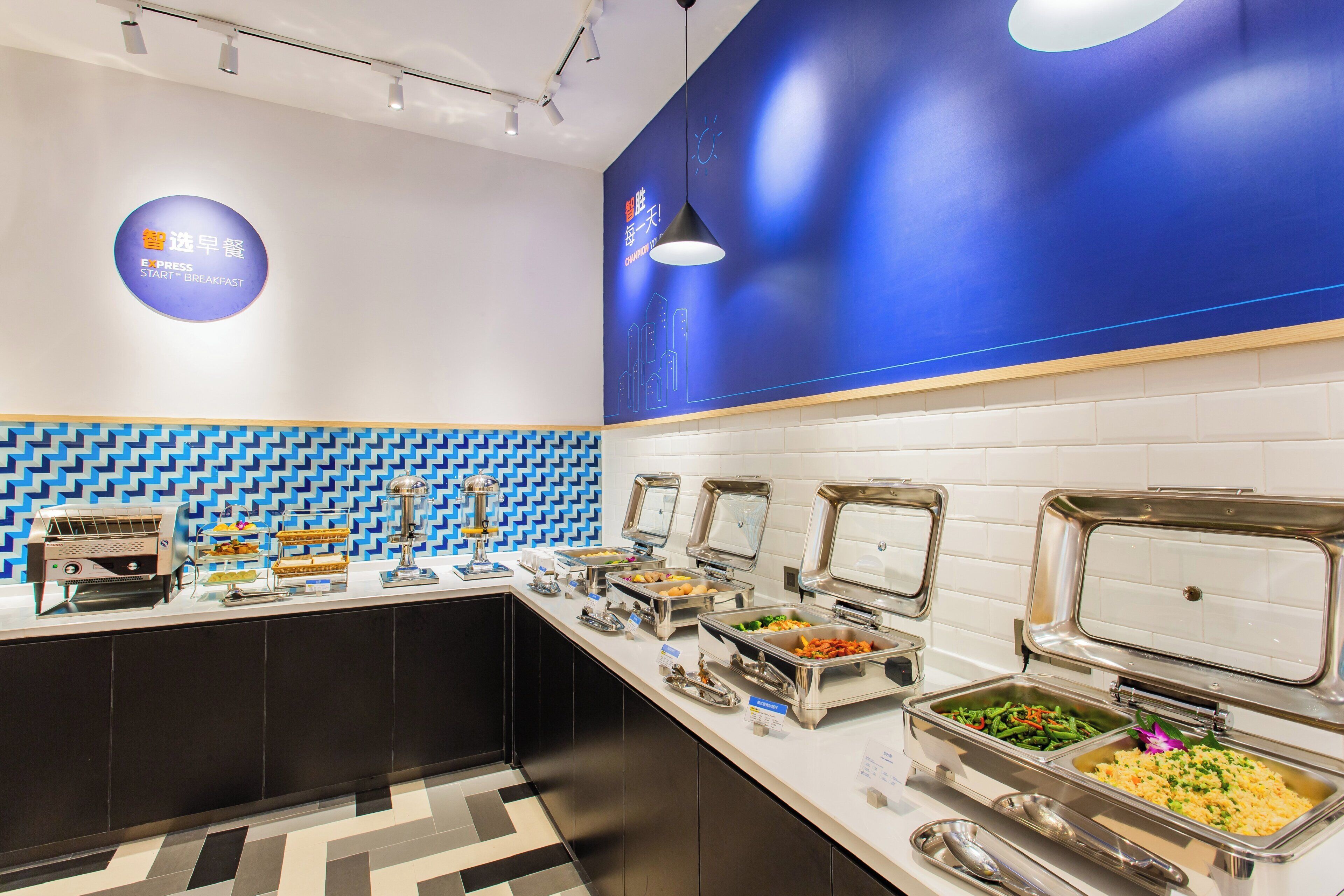 Zona de buffet con varias estaciones de comida, una máquina de café y un reloj en la pared.