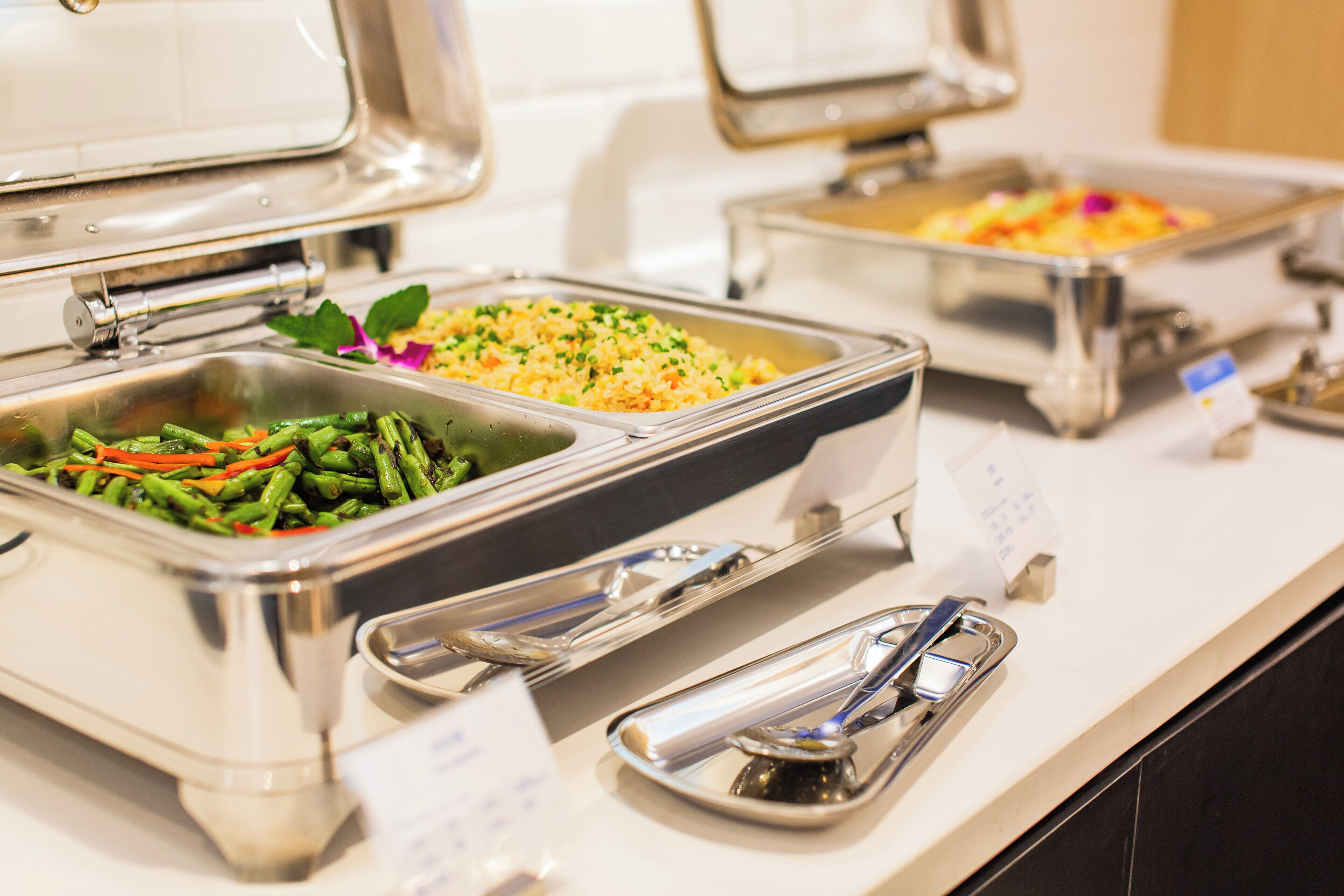 A buffet with various food options, including a dish with green beans and carrots, a rice dish, and a yellow rice dish with vegetables.